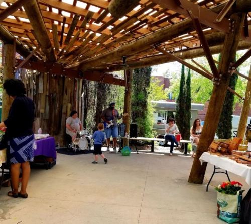 A lively outdoor gathering with musicians playing, people socializing, and tables set with food and decorations.