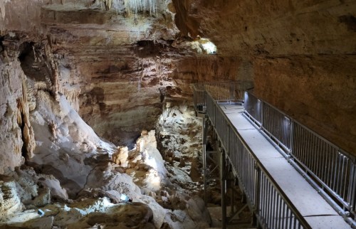 A rocky cave interior with a metal walkway and natural light illuminating the stone formations.