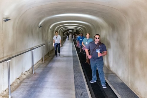 A group of people walking through a long, well-lit tunnel with smooth walls and a flat walkway.