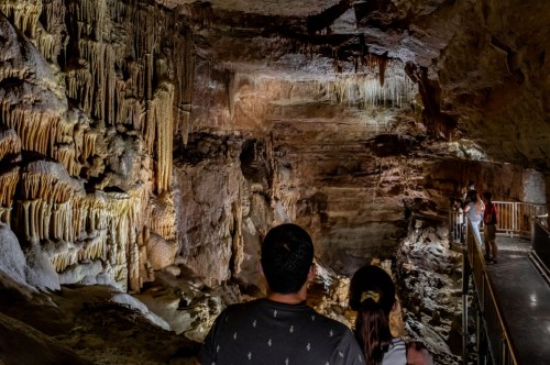 Visitors explore a stunning cave with illuminated stalactites and stalagmites, surrounded by rocky formations.