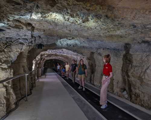 A group of people walking on a path inside a rocky underground tunnel with dim lighting.