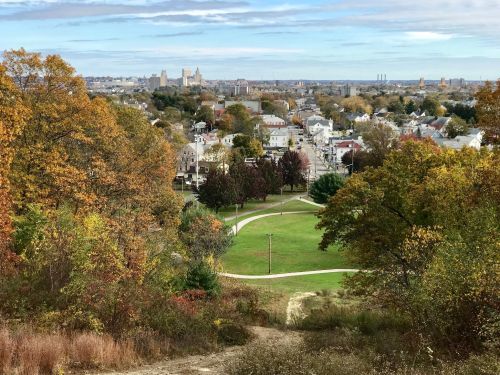 A scenic view of a city skyline surrounded by autumn foliage and green parks, showcasing a mix of urban and natural landscapes.
