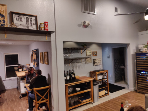Cozy interior of a restaurant with wooden furniture, wine bottles, and patrons enjoying a meal in a warm atmosphere.