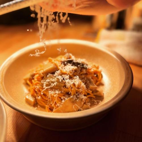 A bowl of pasta topped with grated cheese and mushrooms, with a hand sprinkling more cheese above it.