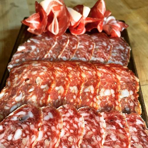 A wooden platter featuring an assortment of sliced cured meats, including salami and prosciutto, arranged neatly.