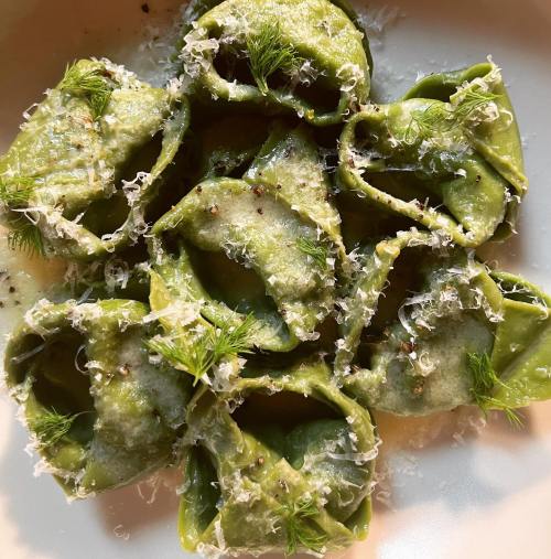 A plate of green tortellini topped with grated cheese, herbs, and black pepper.