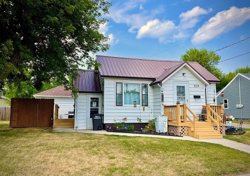 A small, charming house with a metal roof, front porch, and landscaped yard under a blue sky.