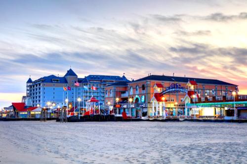 A beachside view at sunset featuring colorful buildings, flags, and a sandy shore.