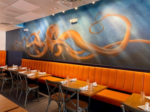 A vibrant mural of an octopus on a blue wall above orange booths in a modern restaurant setting.