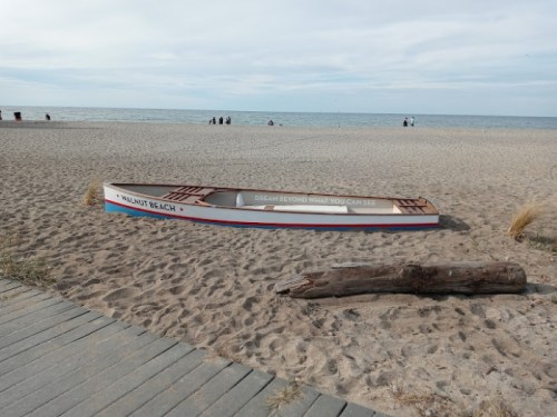 A colorful boat on a sandy beach with a message, surrounded by a calm sea and distant beachgoers.