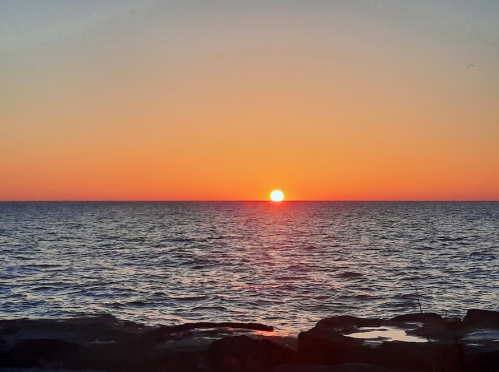 A vibrant sunset over the calm ocean, with warm orange and yellow hues reflecting on the water.