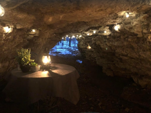 A cozy cave interior with string lights, a lantern, and a table, creating a warm atmosphere in a natural setting.