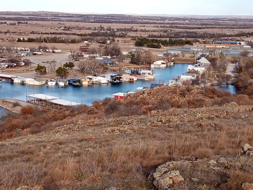Aerial view of a marina with houseboats along a winding river, surrounded by grassy hills and open fields.