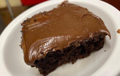 A slice of chocolate cake with smooth chocolate frosting on a white plate.