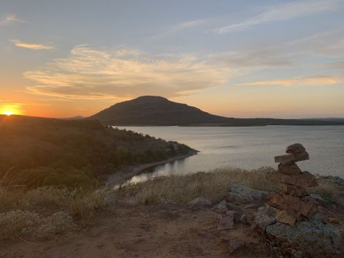 Sunset over a lake with a mountain in the background and a small rock formation in the foreground.