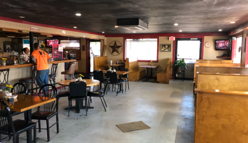 Interior of a casual restaurant with wooden booths, tables, and a bar area. A few patrons are seated.