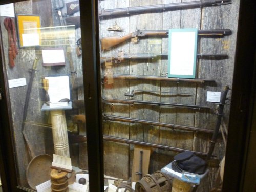 Display case featuring various historical firearms and artifacts against a wooden background.