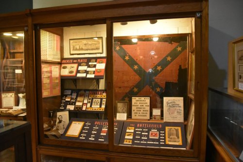 Display case featuring historical artifacts, including a Confederate flag, buckles, and battlefield memorabilia.