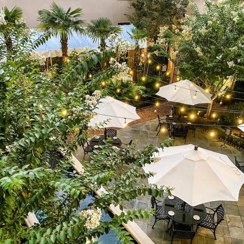 A lush garden with palm trees, white umbrellas, and string lights illuminating outdoor dining tables.