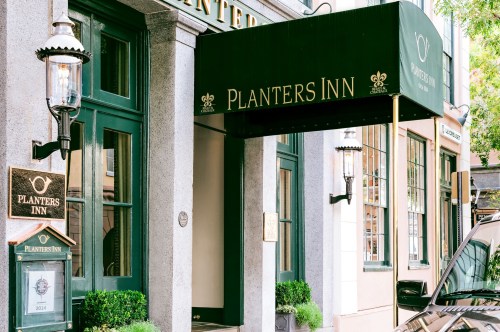 Entrance of Planters Inn with a green awning and decorative signage, surrounded by potted plants and elegant architecture.