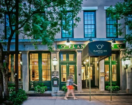 A charming hotel entrance with green accents, large windows, and a canopy reading "Planters Inn" surrounded by trees.