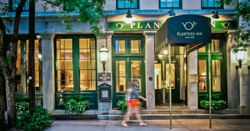 A person walks past the entrance of Planters Inn, featuring green awnings and decorative lanterns.