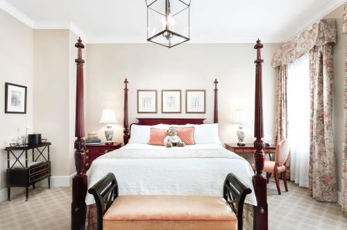 Cozy bedroom with a four-poster bed, decorative pillows, a teddy bear, and elegant furnishings. Soft lighting and floral accents.