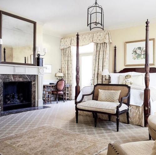 A cozy bedroom featuring a four-poster bed, elegant furnishings, a fireplace, and soft floral decor.
