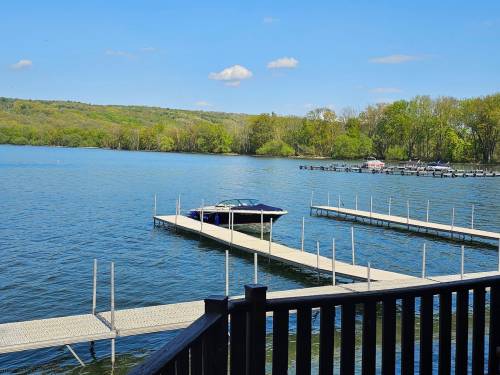 A serene lake view with a boat docked on a sunny day, surrounded by lush greenery and blue skies.