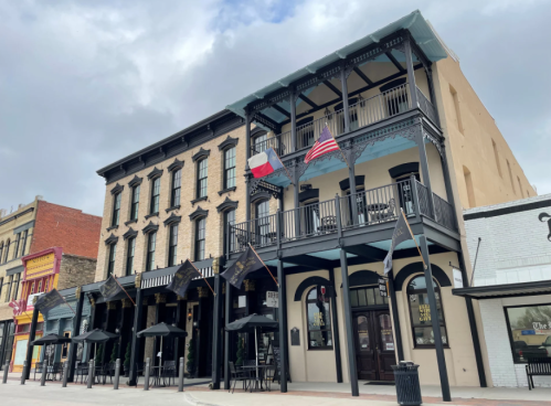 Historic building with balconies, flags, and outdoor seating in a vibrant urban setting.