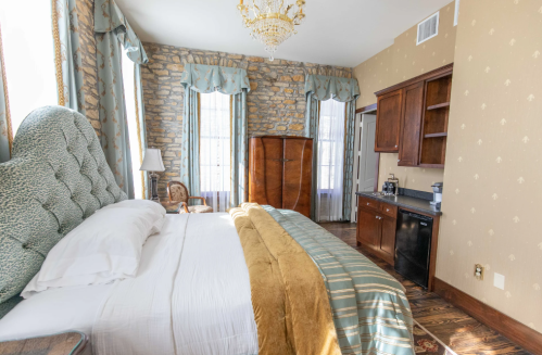 Cozy bedroom featuring a stone wall, a large bed with a gold throw, and wooden furniture, including a mini fridge.