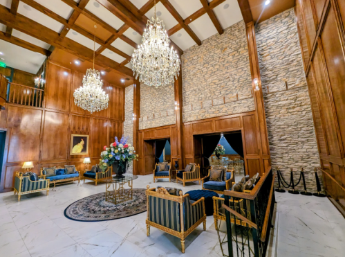 Elegant lobby with wooden walls, stone accents, chandeliers, and plush seating, featuring a large floral arrangement.