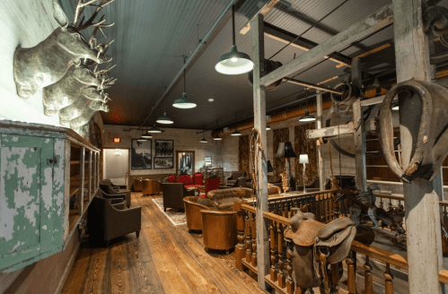 Rustic interior with mounted deer heads, wooden floors, and cozy seating areas in a lodge-like setting.