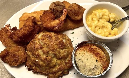 A plate of fried shrimp, crab cake, hush puppies, and macaroni and cheese, served with a side of cornbread.