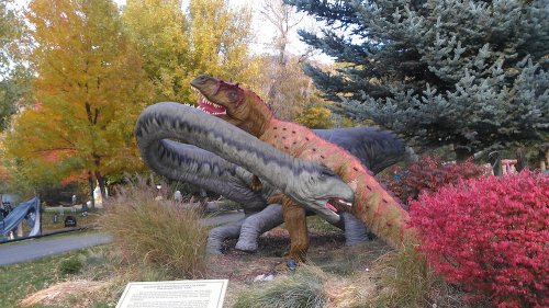 A colorful dinosaur sculpture with long necks and vibrant foliage in the background, set in a park.