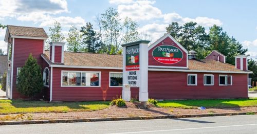 Exterior of Pasta More restaurant, a red building with a sign, surrounded by trees and a clear blue sky.