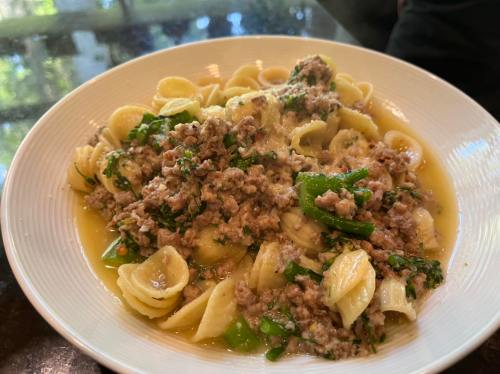 A plate of pasta with ground meat, green peppers, and herbs in a light sauce, served steaming hot.