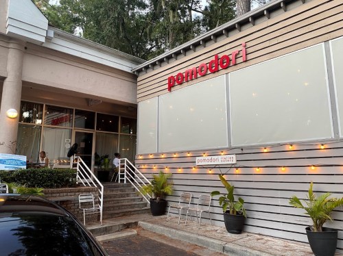 Exterior of Pomodori restaurant with a welcoming entrance, outdoor seating, and decorative lights.