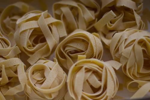 Close-up of uncooked fettuccine pasta arranged in neat, spiral nests on a light background.