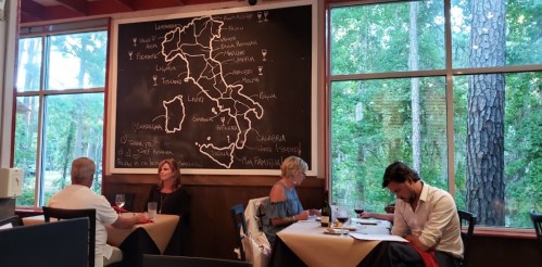 A cozy restaurant interior with a large chalkboard map of Italy and diners at tables enjoying their meals.