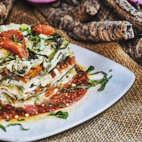 A delicious slice of vegetable lasagna topped with fresh herbs and served on a white plate.