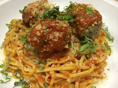 A plate of spaghetti topped with three meatballs, marinara sauce, and garnished with chopped herbs.