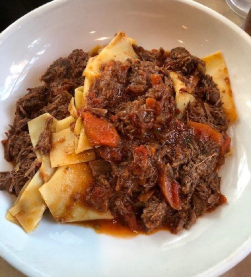 A bowl of pasta topped with shredded beef and a rich tomato sauce, garnished with pieces of tomato.