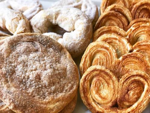 A variety of pastries, including sugar-dusted rounds and flaky, spiral-shaped pastries, arranged on a plate.