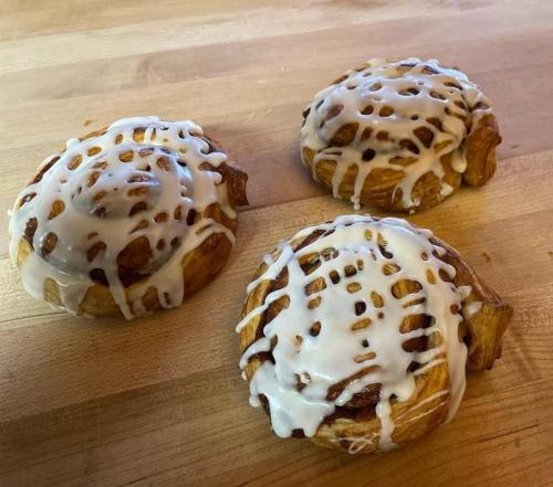 Three cinnamon rolls with white icing on a wooden surface.