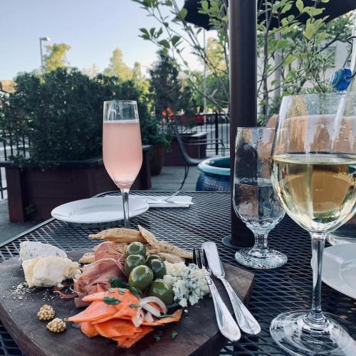 A charcuterie board with meats, cheeses, olives, and crackers, accompanied by glasses of pink and white drinks on a patio.