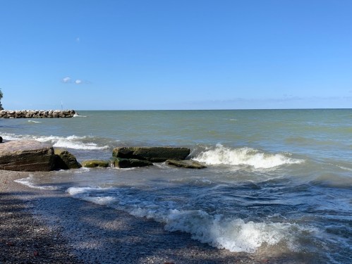 A serene lakeshore scene with gentle waves lapping against rocky formations under a clear blue sky.