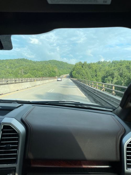View from inside a car on a highway, with green hills and a blue sky in the background.