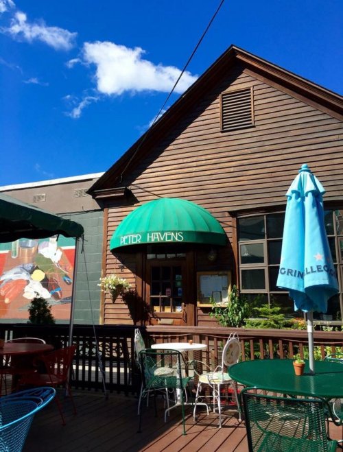 A charming wooden building with a green awning, outdoor seating, and a blue sky in the background.