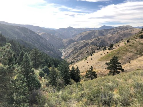 A scenic view of rolling hills and valleys, dotted with trees under a partly cloudy sky.